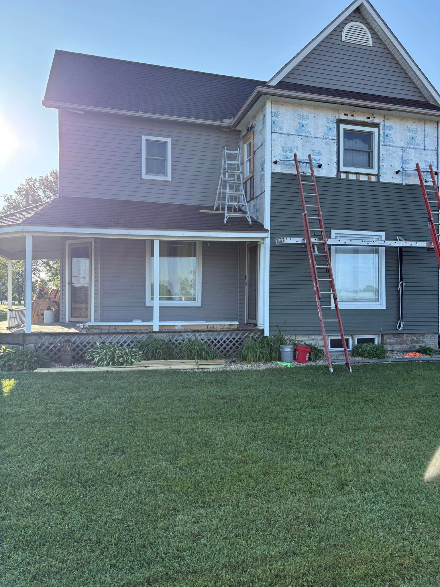Two-story gray house with red ladder leaning against the front and a green lawn in front.