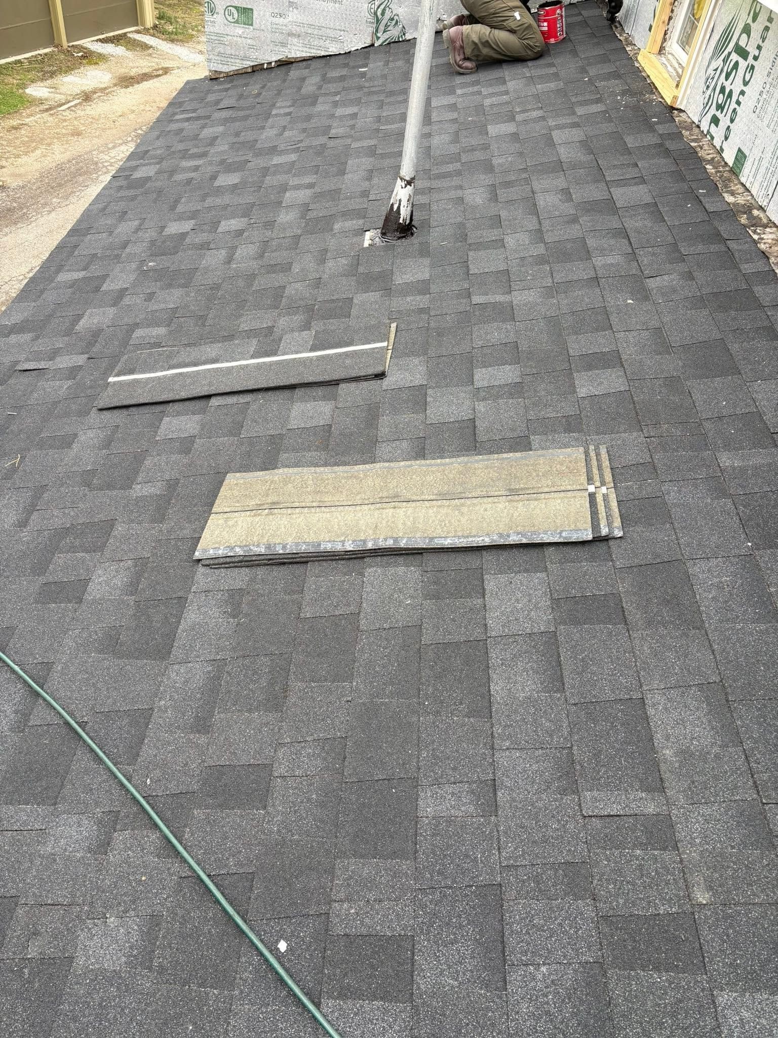 Gray roof shingles with two boards and a pole laying across the surface