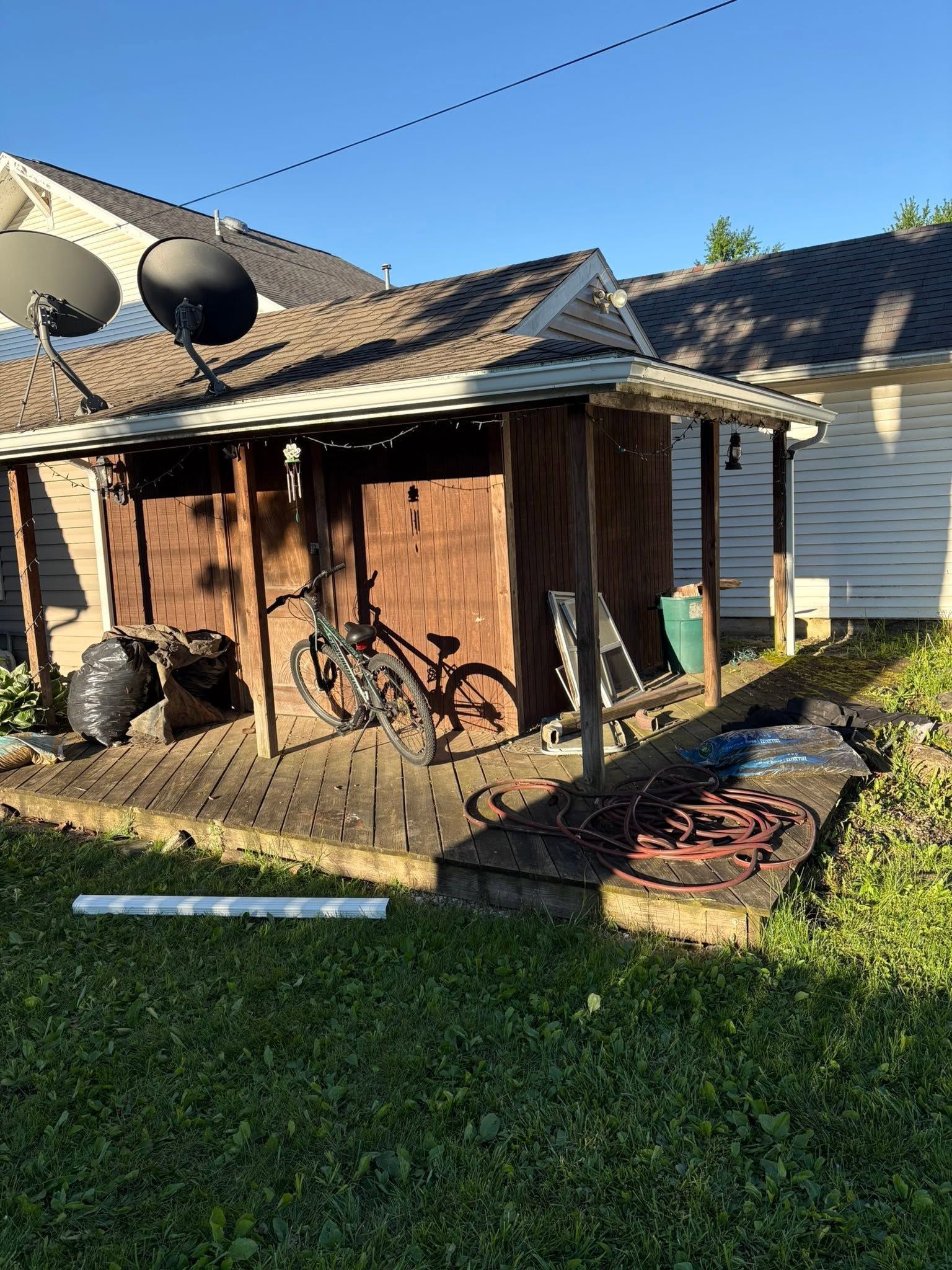 Backyard shed with damaged roof, leaning bicycles, and scattered debris beside a white house.