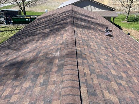 Roof shingles on a house, viewed from the ridge with a vent and driveway in the background
