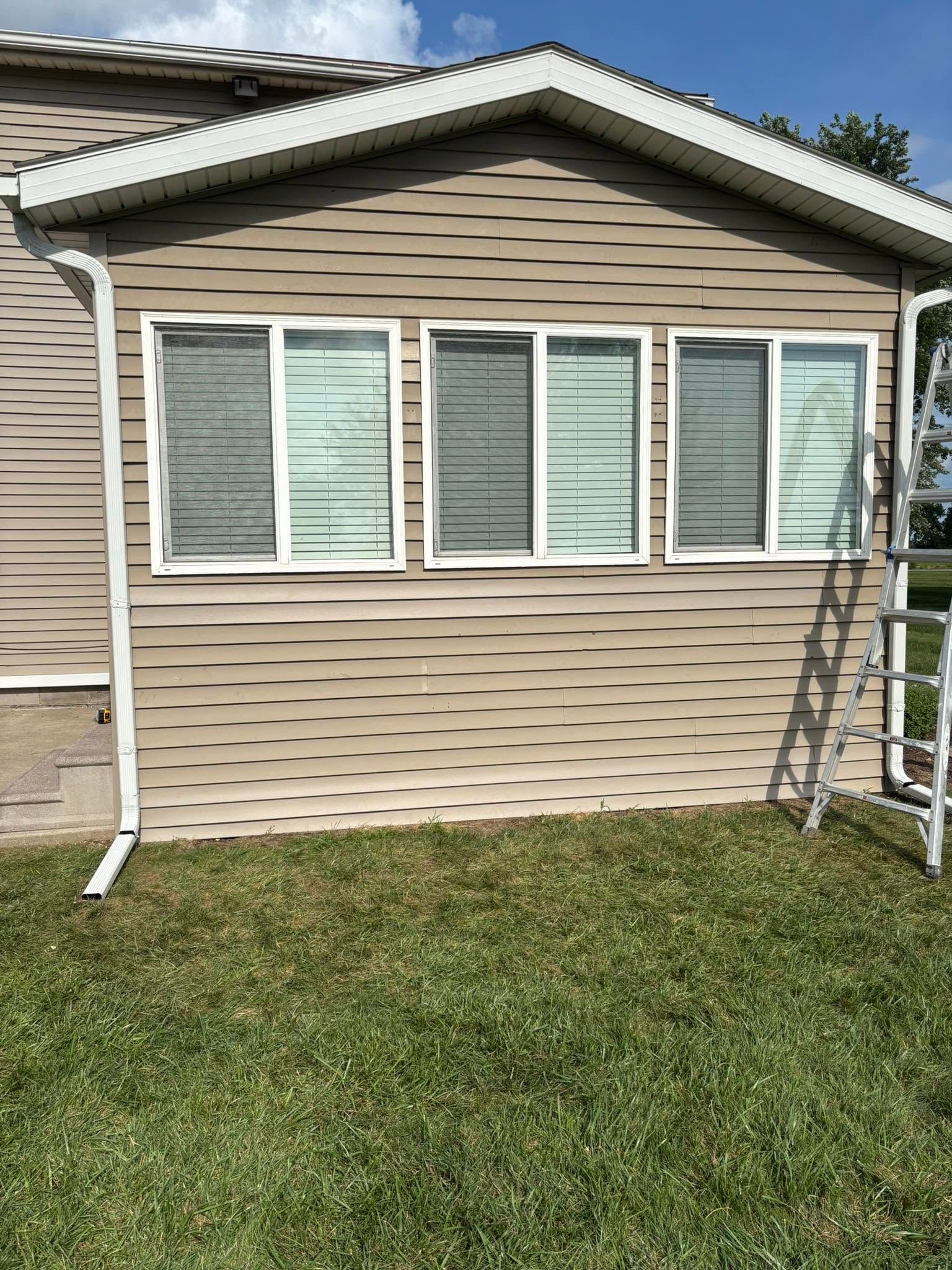 House exterior with three front windows and a ladder leaning on the right side above a grassy yard