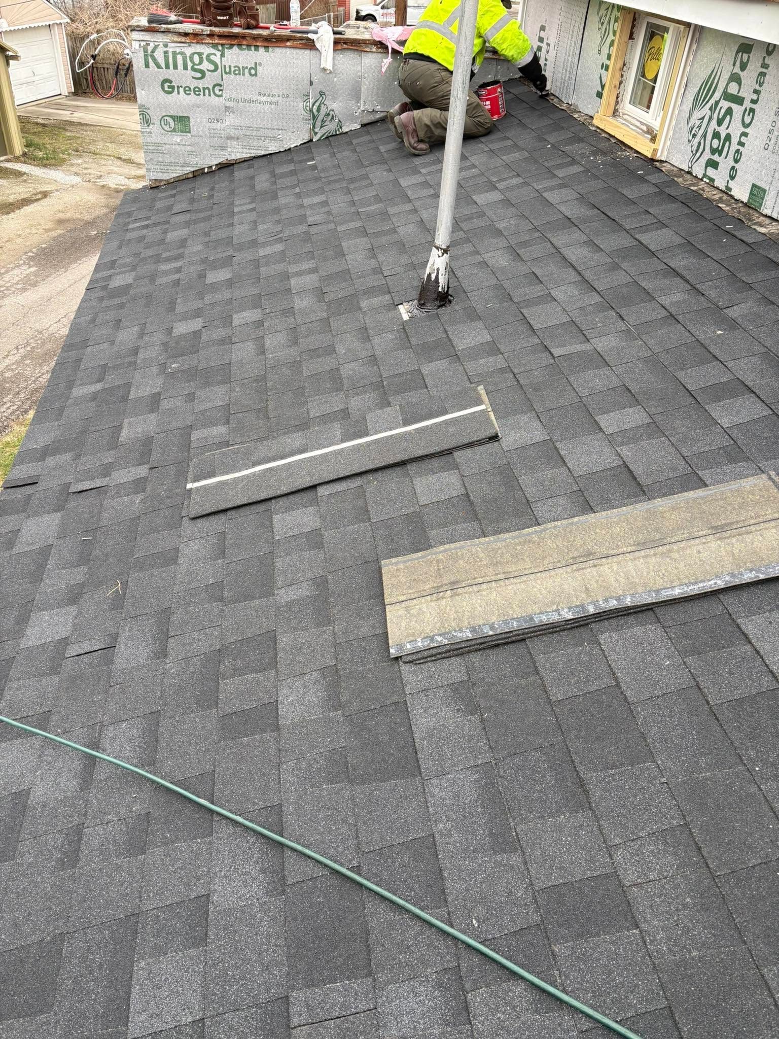 Rooftop under construction with dark shingles, a vent pipe, and tools on the roof.