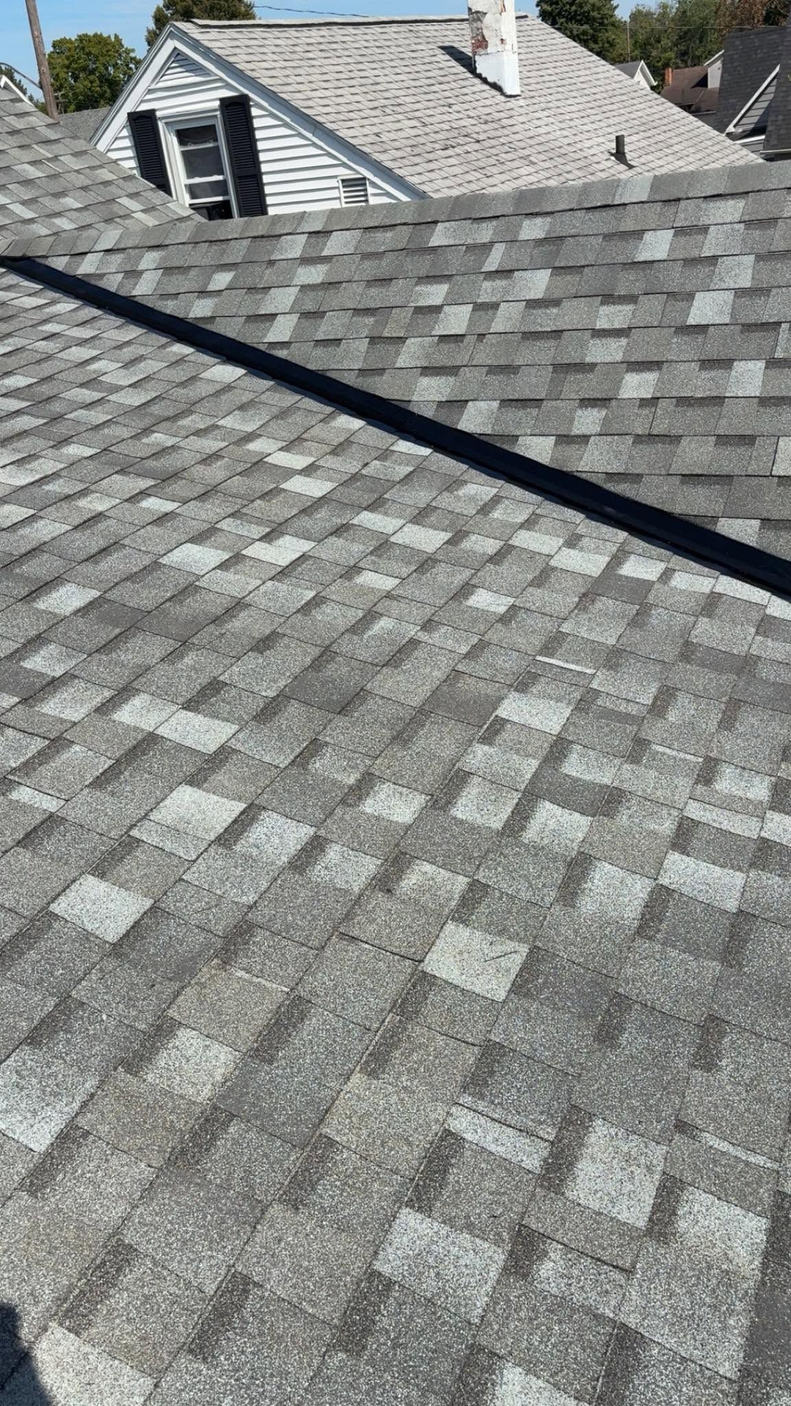 Gray shingle roof with skylight and neighboring rooftops under bright daylight
