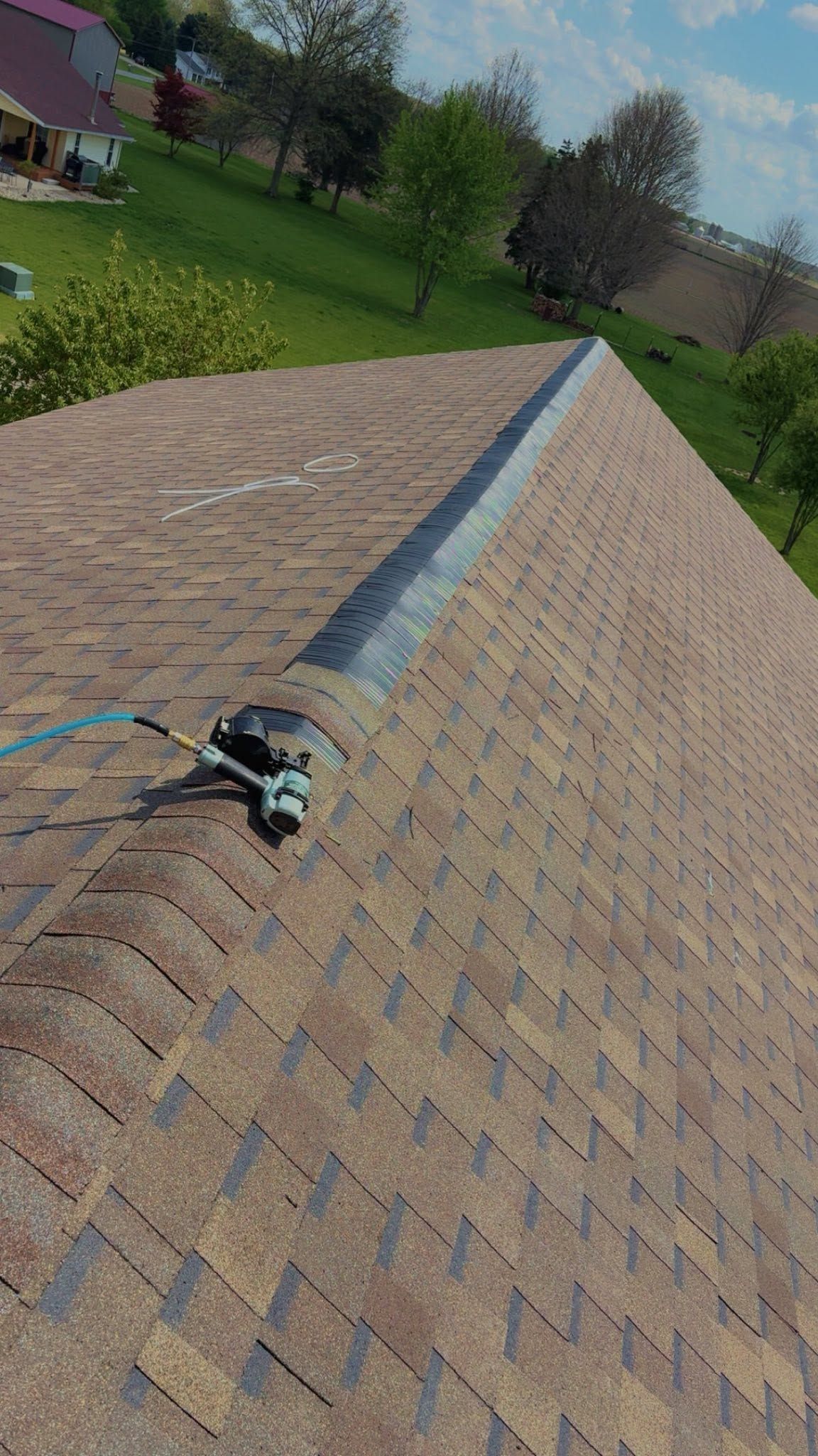 Close-up of a roof with a long blue ridge vent and a power tool on brown shingles.