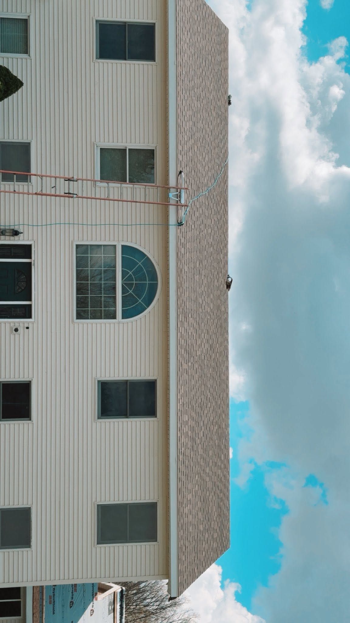 Tall beige apartment building with many windows against a blue sky with clouds.