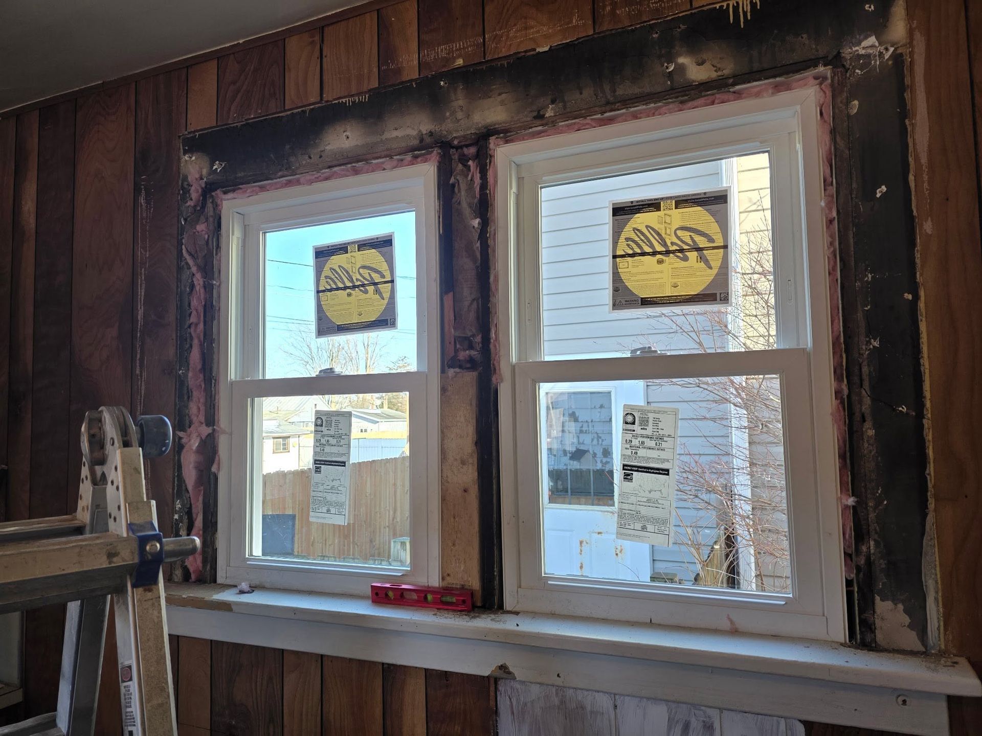 Wooden wall with two windows, yellow signs taped inside, and a small shelf below.