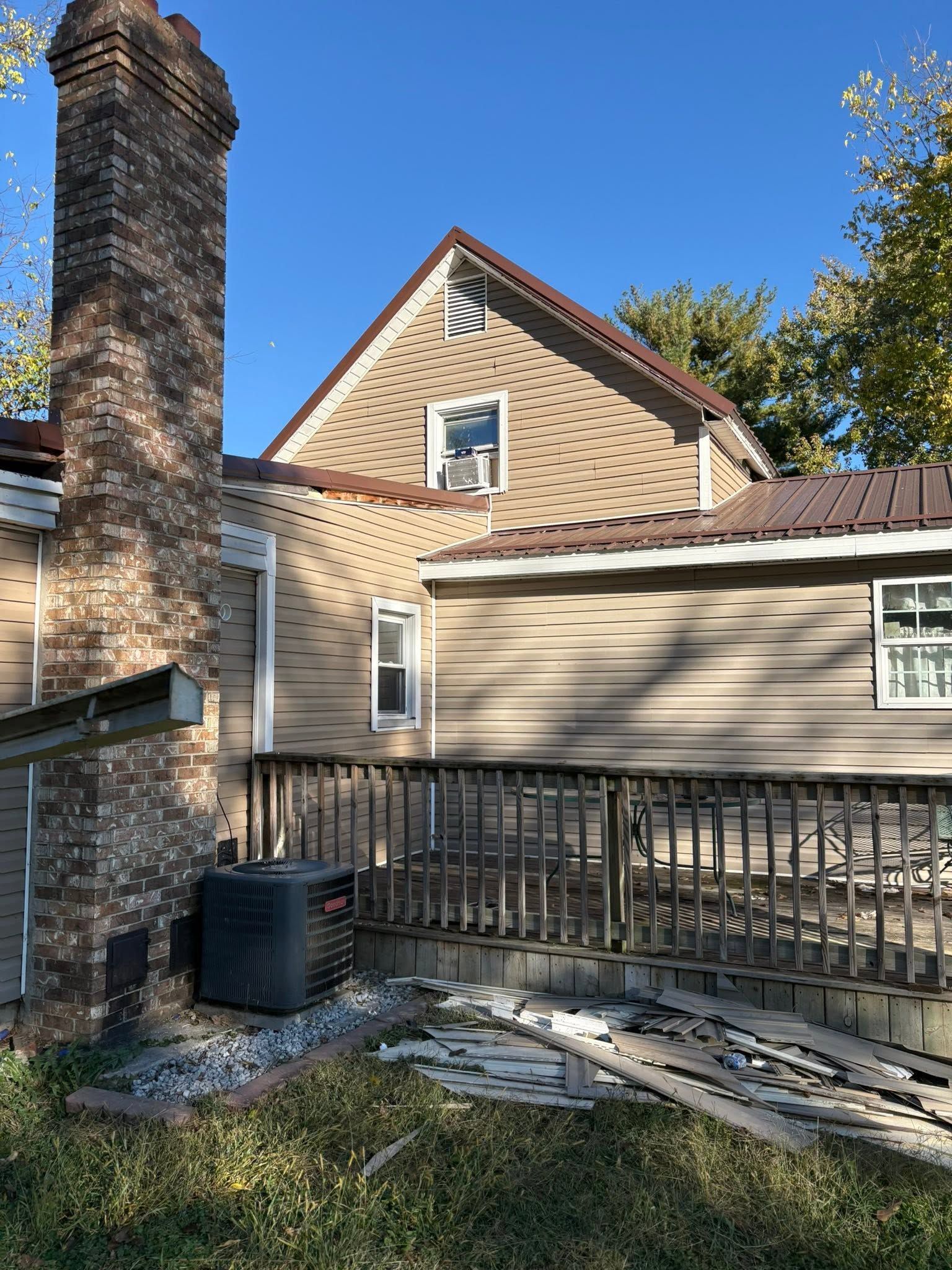 Brick house exterior with chimney, tan siding, and fenced patio under a clear blue sky