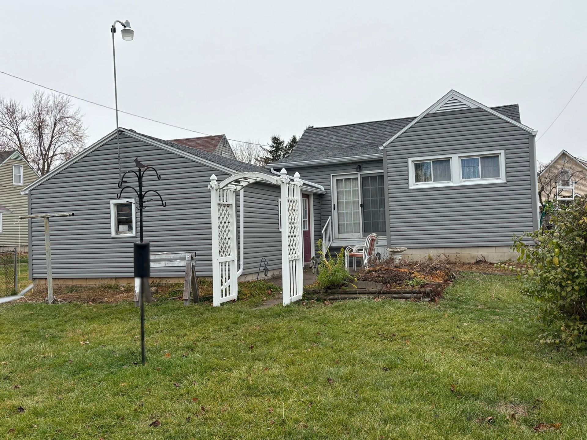 Gray house with white trim and a small white arbor in a grassy yard
