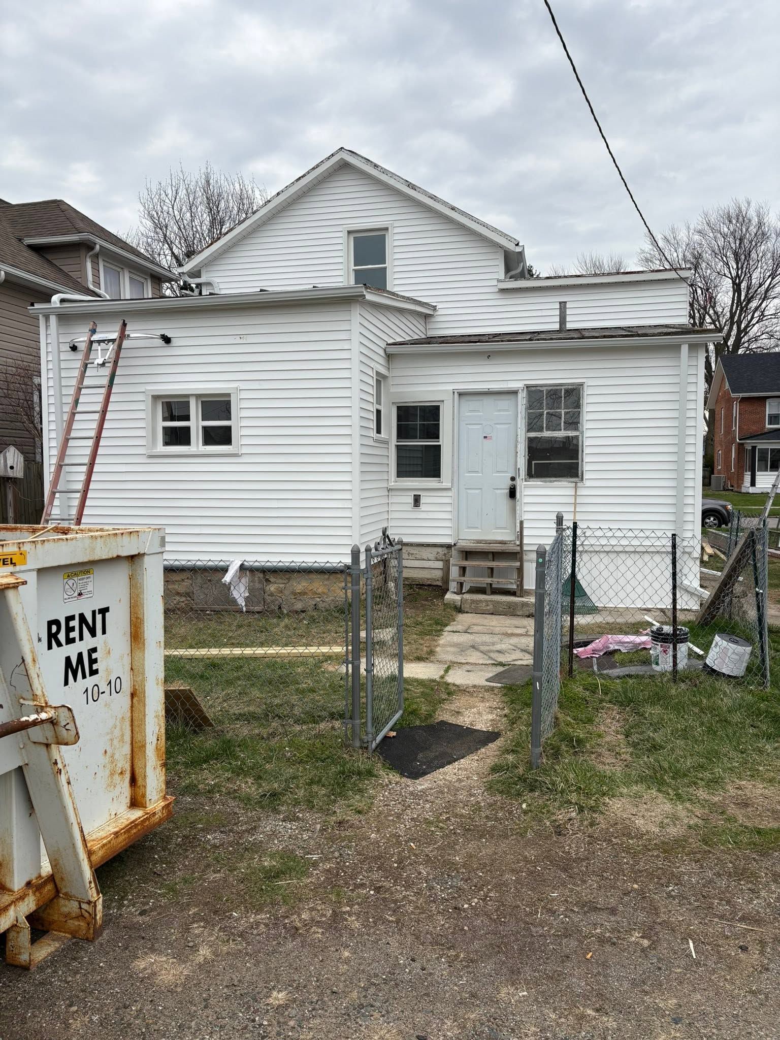 Small white house with a chain-link fence and a “RENT ME” sign in the yard.