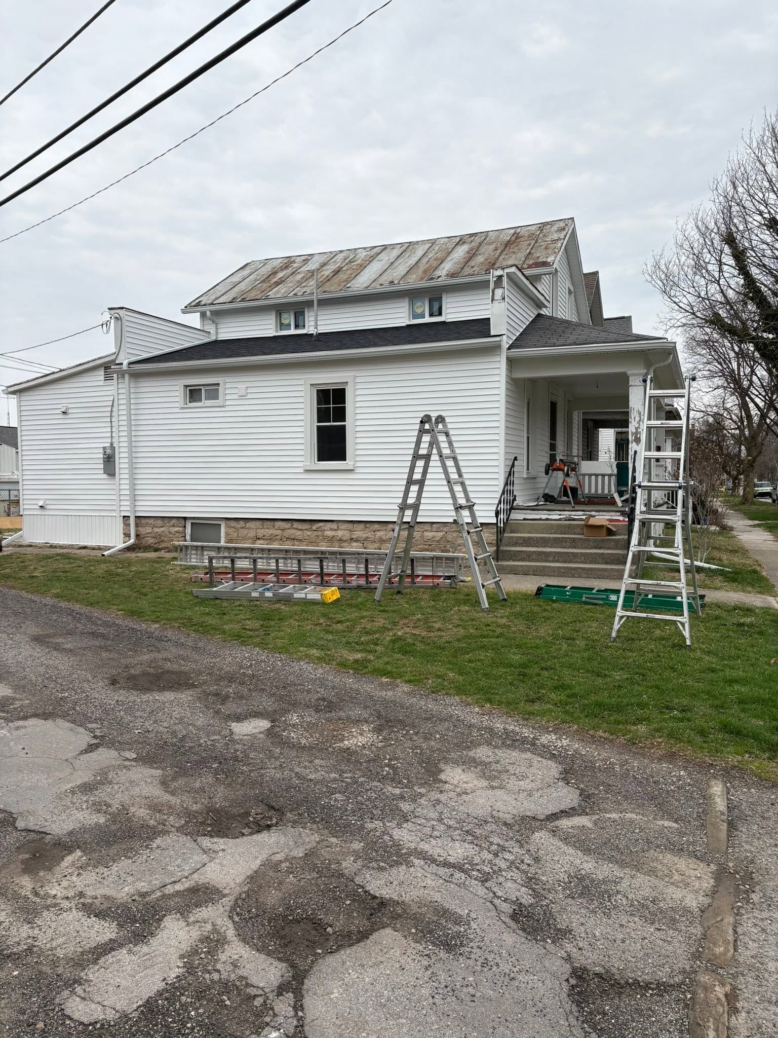 White house under repair with ladders and construction materials along the front porch and roof.