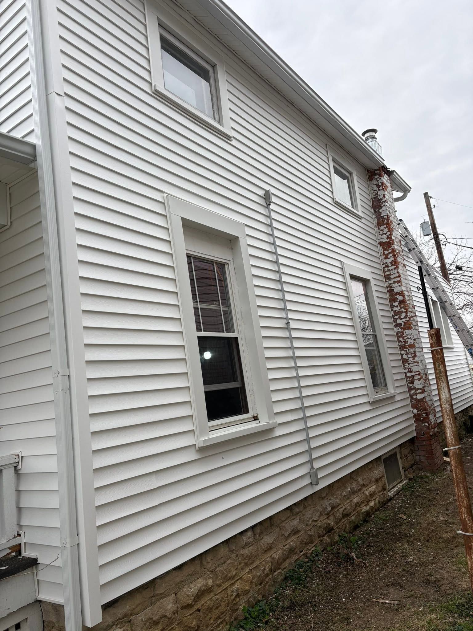 White house siding with two windows and a vine-covered trellis along the side yard