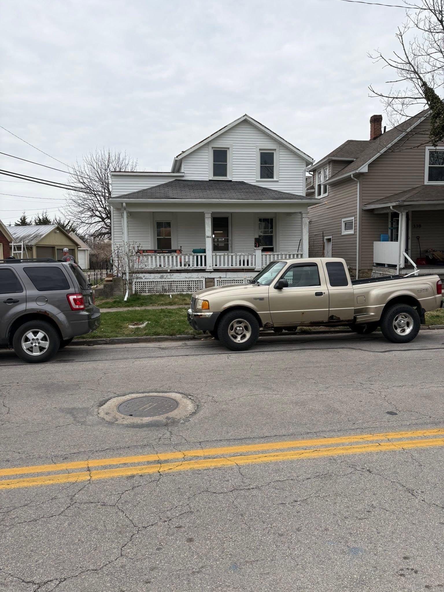 Street view of a white house with two parked pickup trucks along the curb