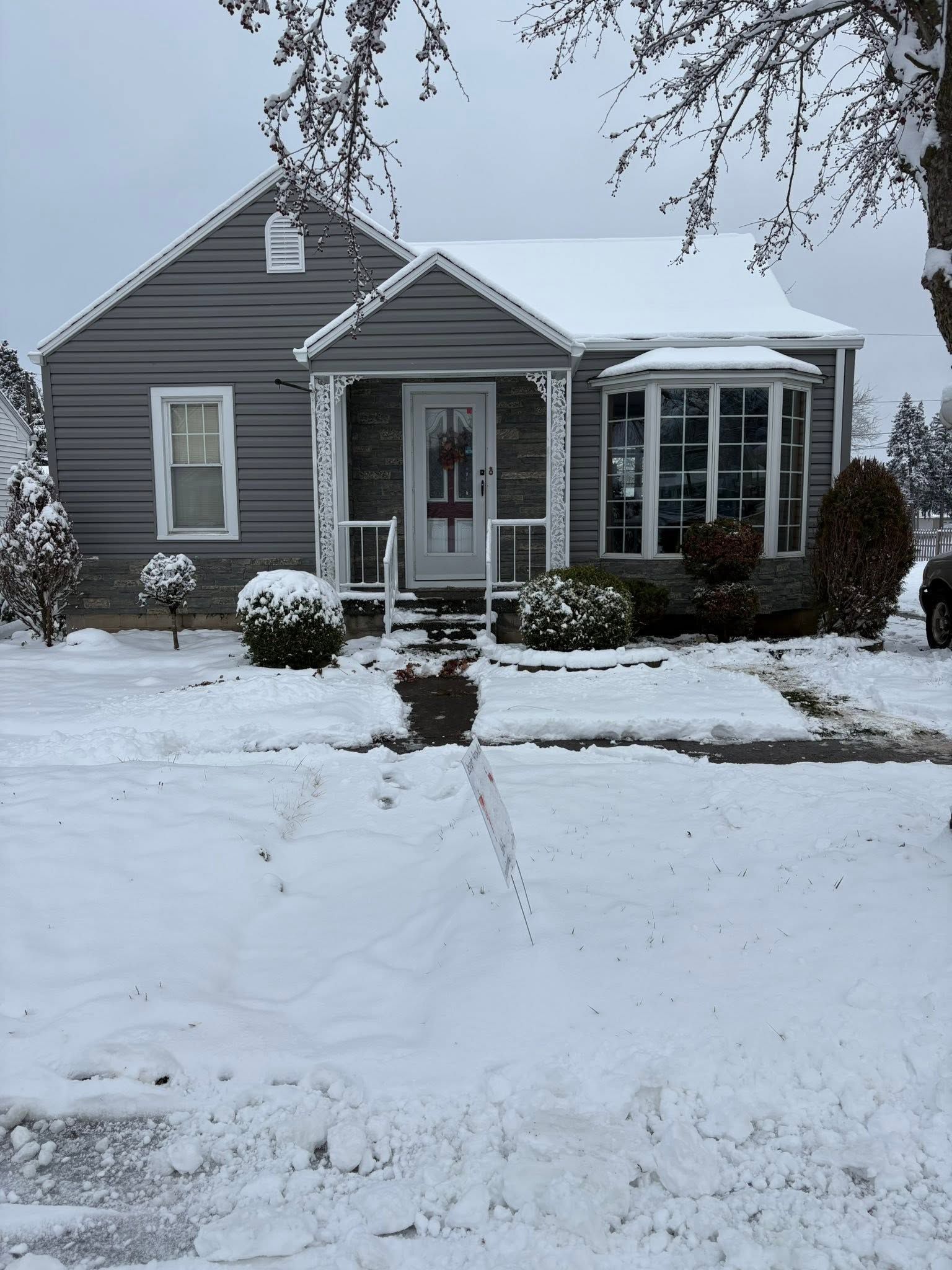 Gray house with a snow-covered yard and driveway in winter.