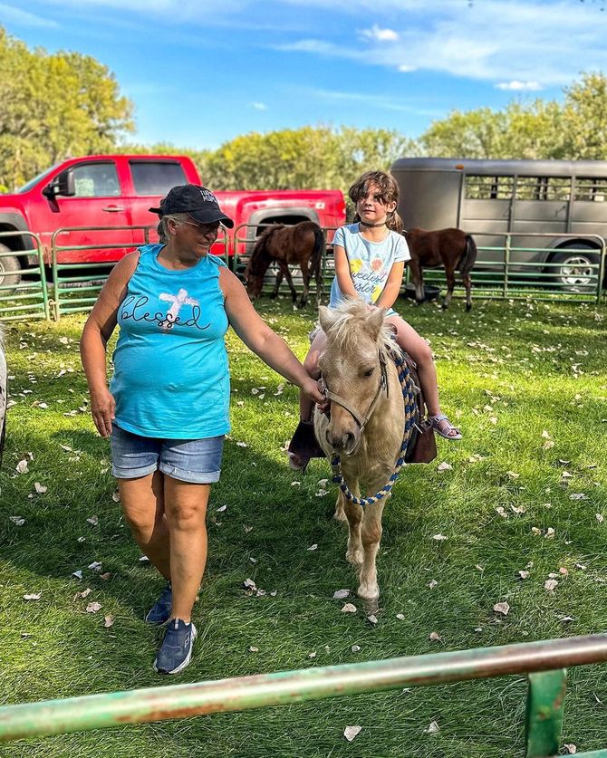 A woman is walking next to a little girl riding a pony.