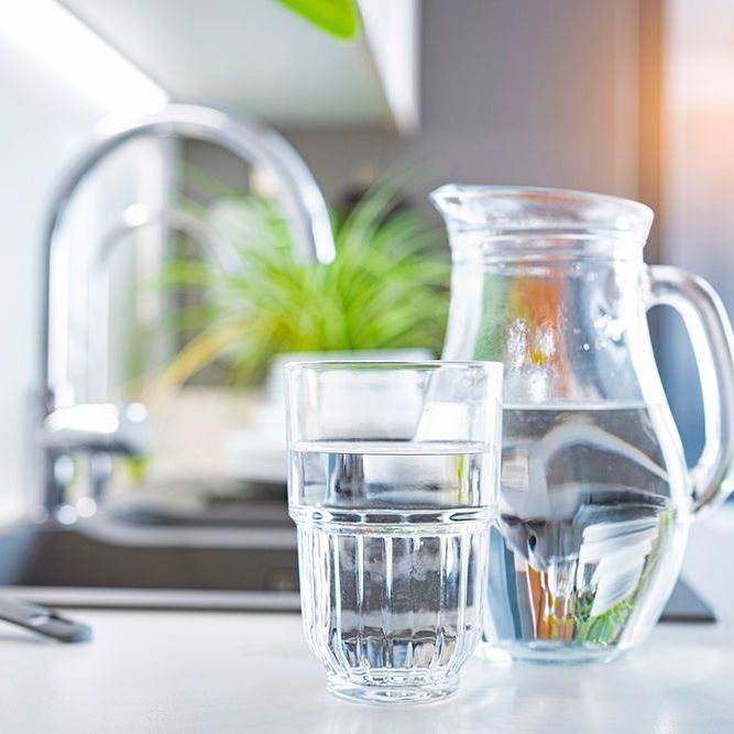 A pitcher of water and a glass of water are on a counter in a kitchen.