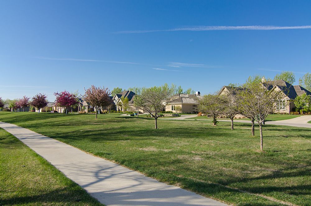 A residential neighborhood with a concrete walkway going through a grassy field.