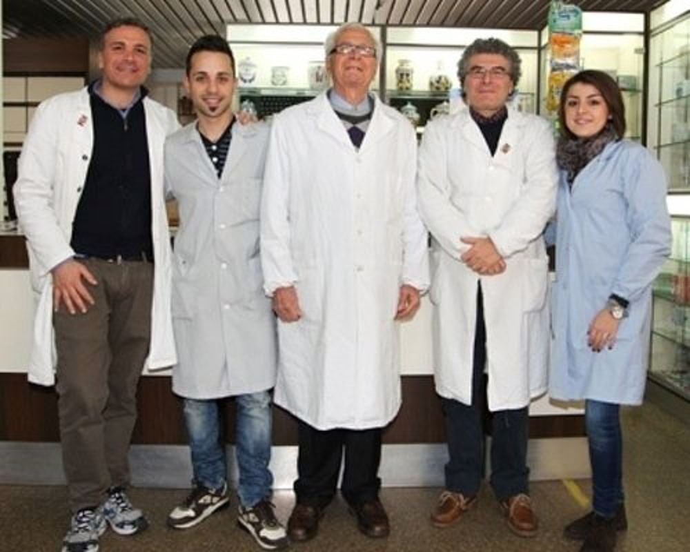 Cinque persone in camice da laboratorio, in piedi insieme in un ambiente interno, in posa davanti a un bancone.