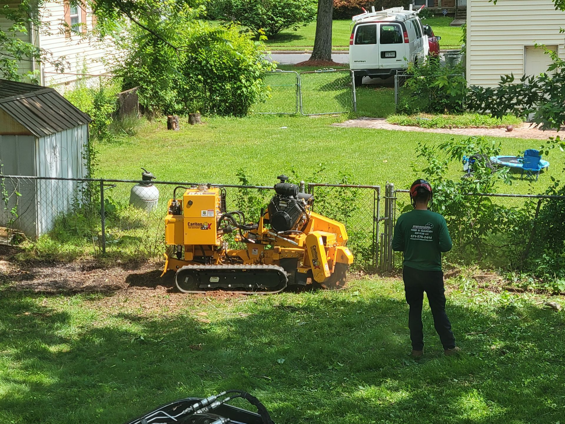 Yellow stump grinder, person in green shirt operating it near a fence in a backyard.