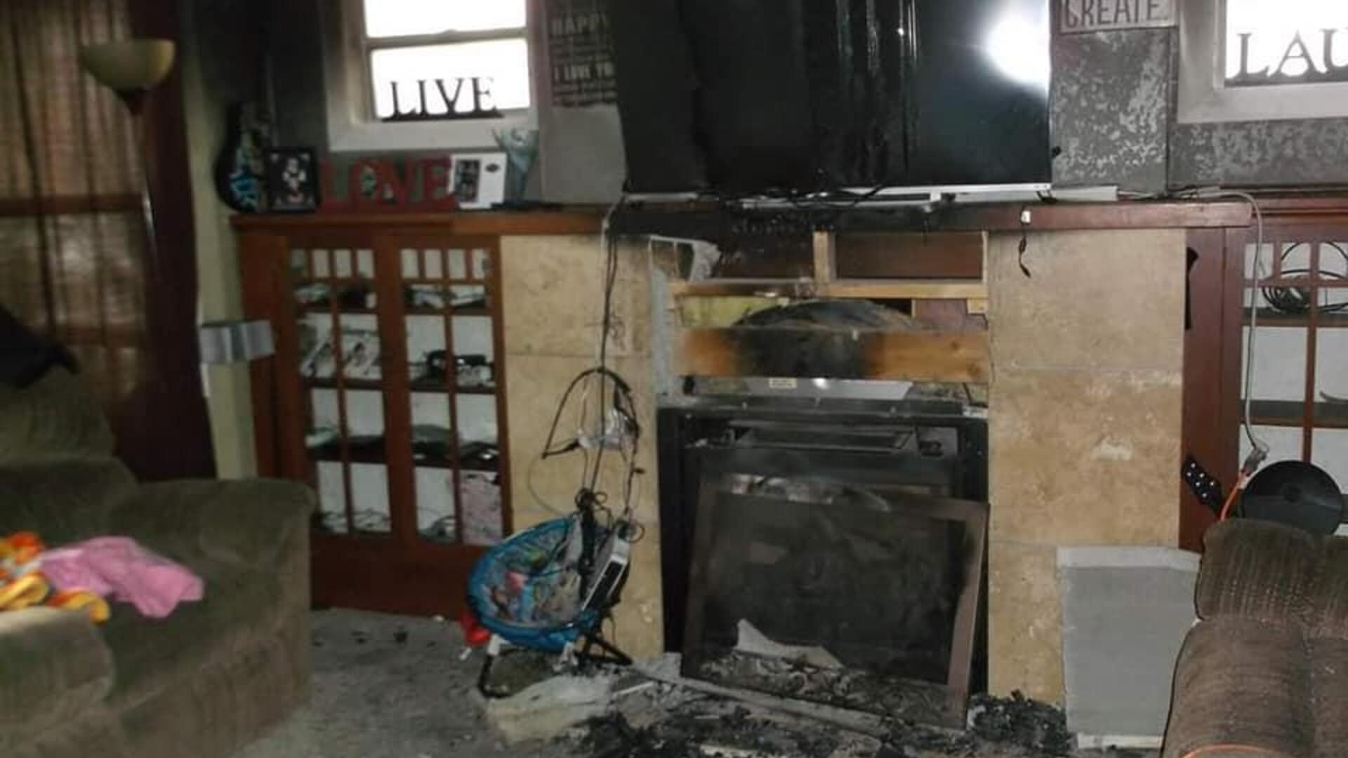 Living room with significant fire damage; charred fireplace, debris, and damaged furniture.