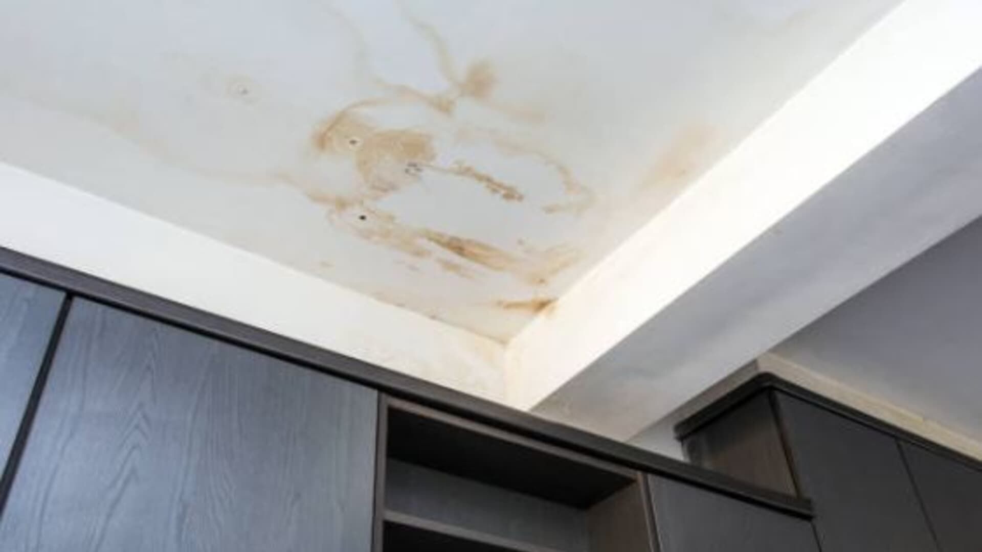 Water-stained ceiling with brown discoloration, likely a leak. Dark cabinetry below, white walls.