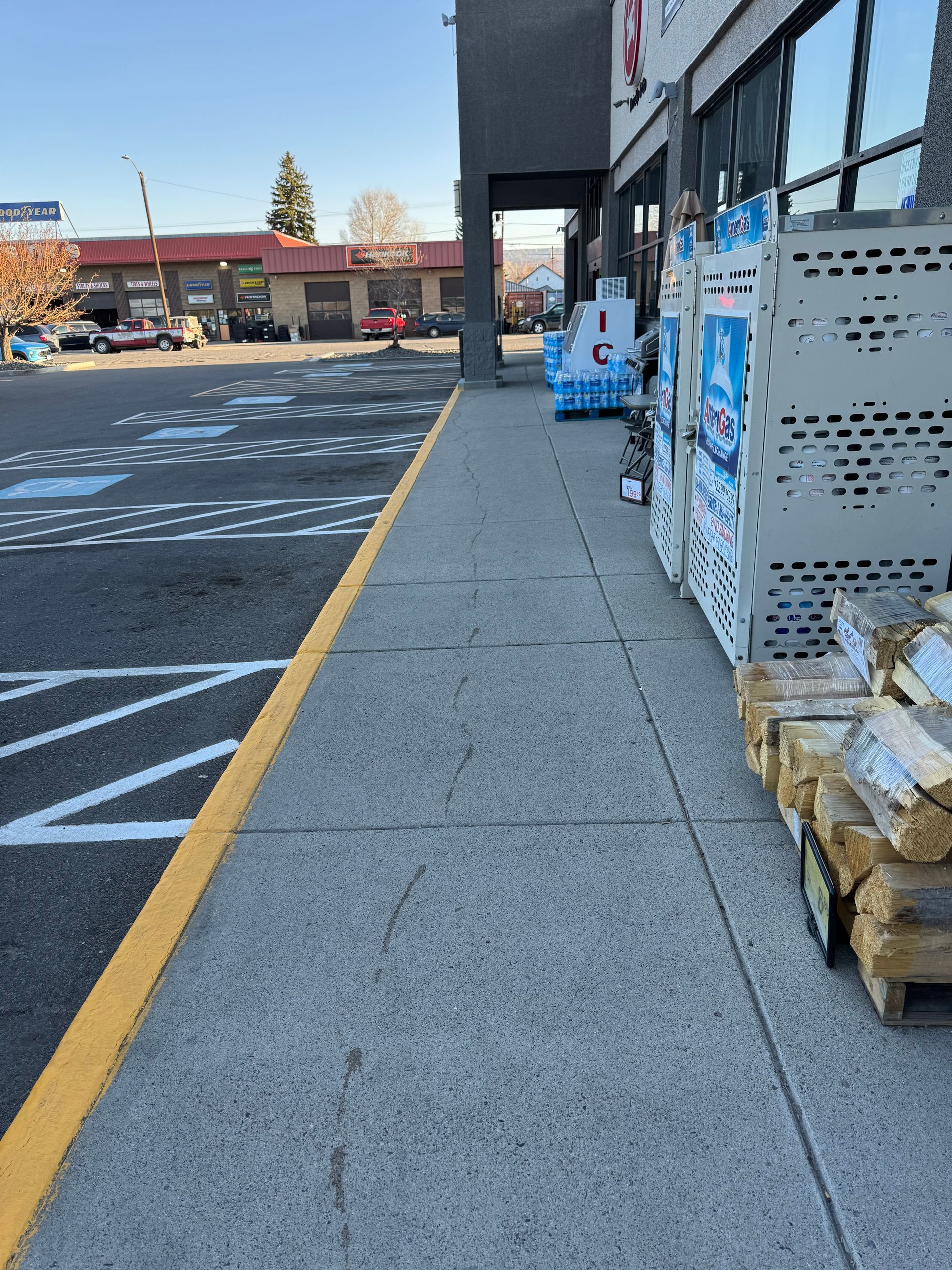 Sidewalk next to a store, with merchandise stacked on the right and parking lot on the left.
