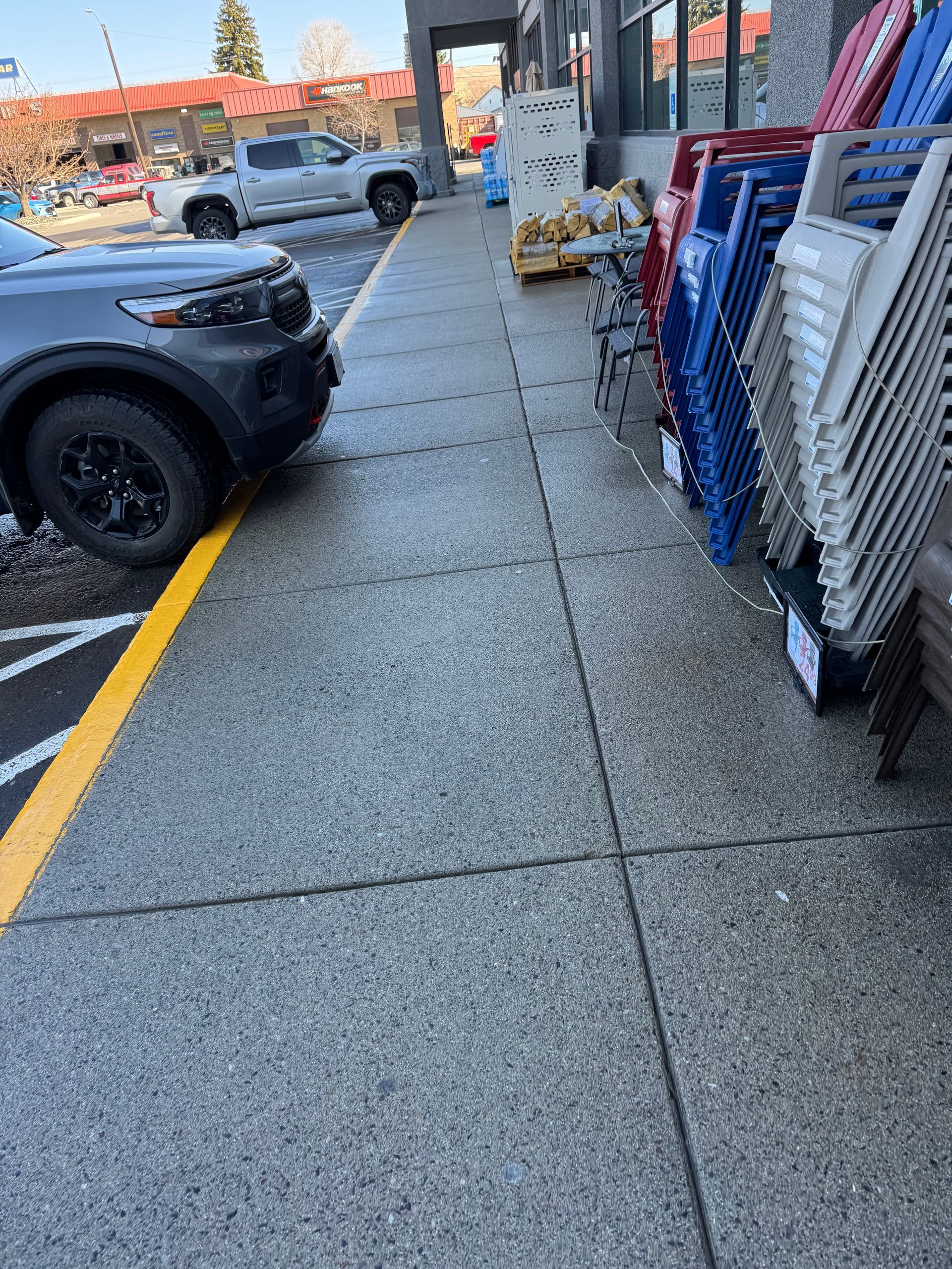 Sidewalk blocked by a vehicle. Plastic chairs lined against building. Yellow curb marking.