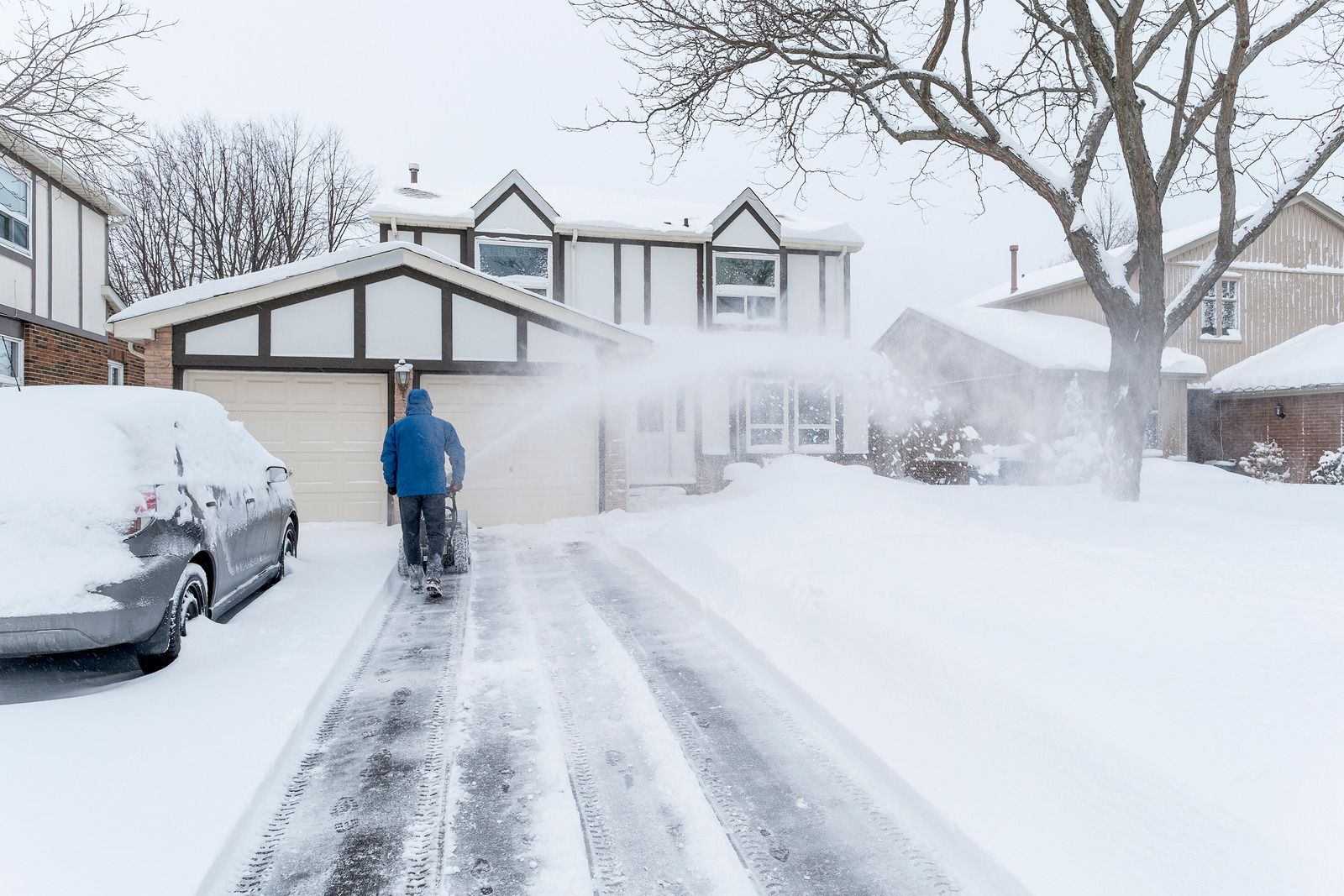 Person operating a snowblower, clearing snow from a white field on a sunny day.