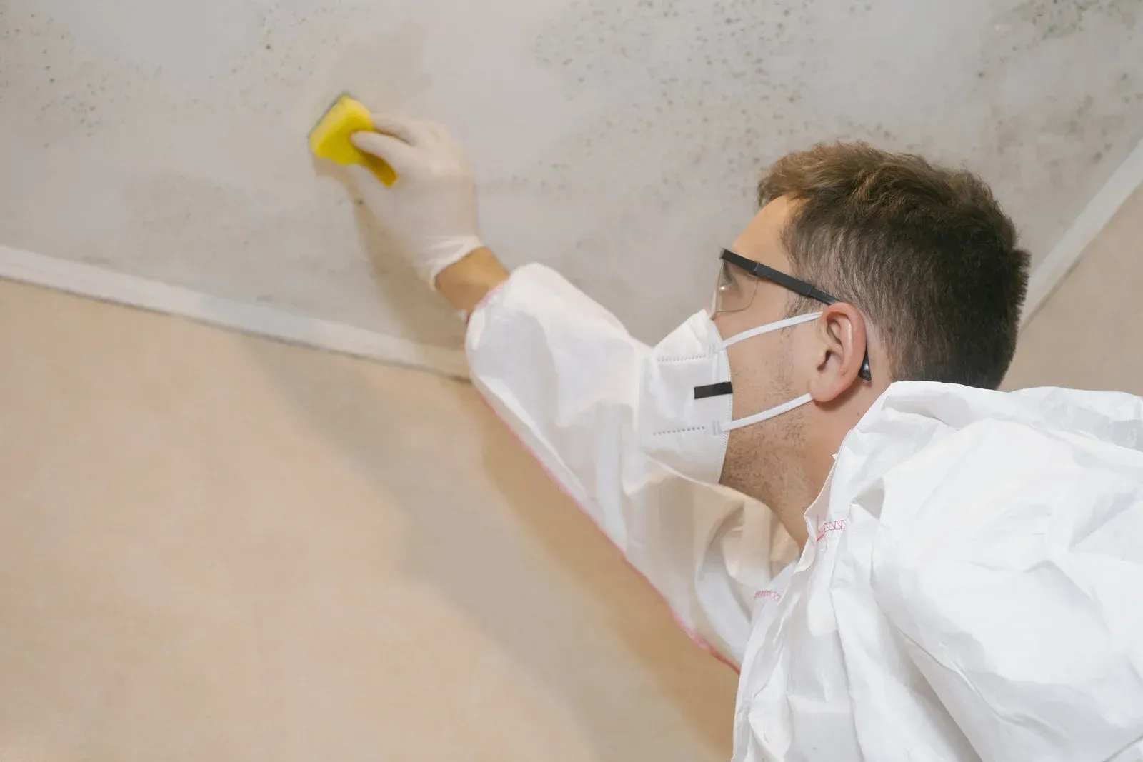 Person in protective gear cleaning mold on a ceiling.