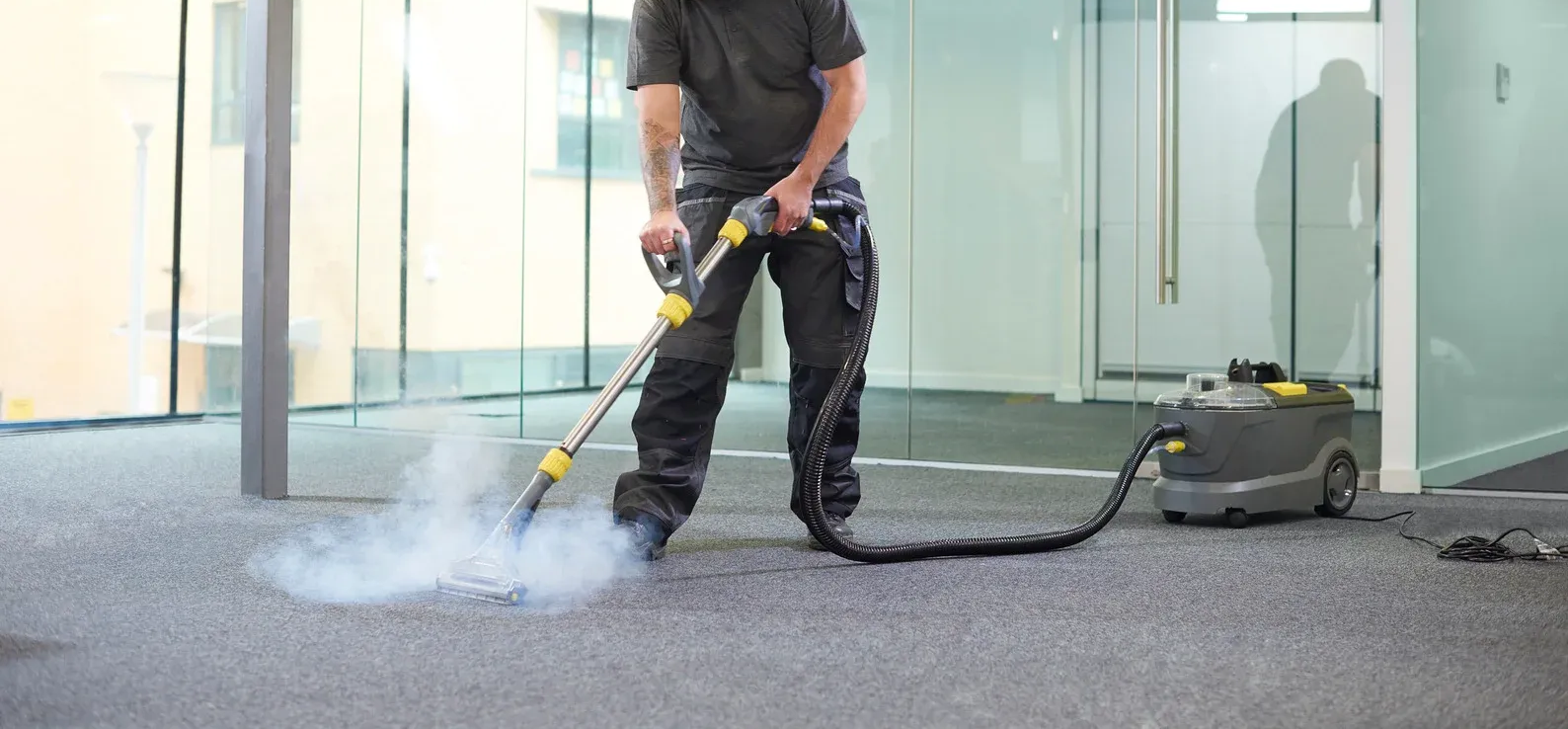 Person wearing blue gloves cleaning a patterned rug with a steam cleaner.