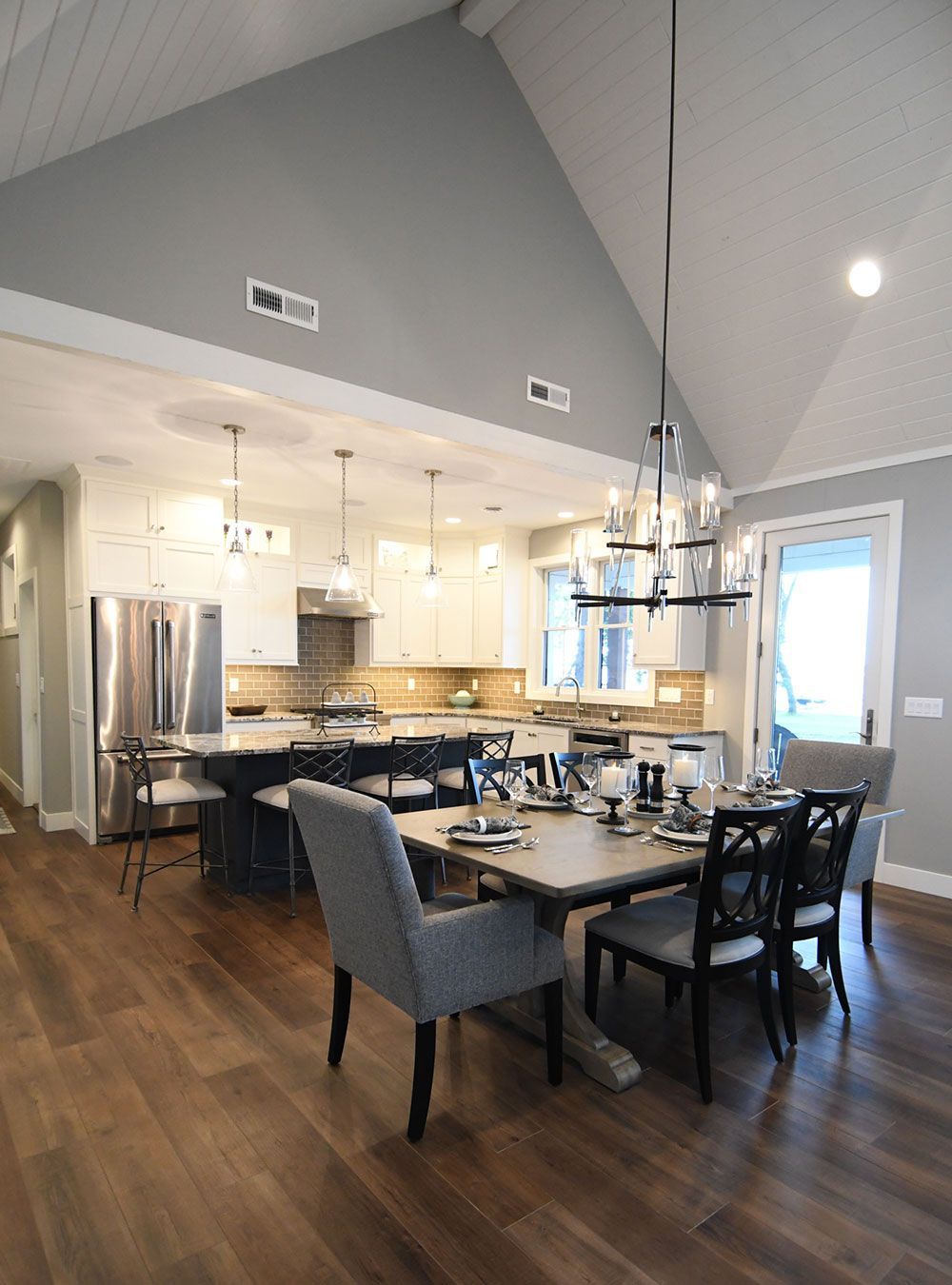 Spacious kitchen and dining area. Wooden floors, gray walls, white cabinets, dark dining set, chandelier.