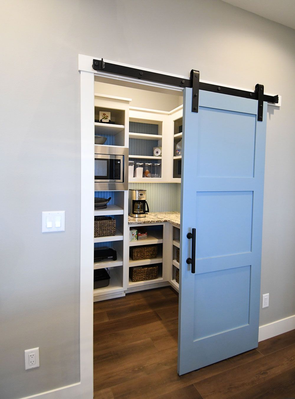 Light blue barn door to a pantry with shelves and appliances.