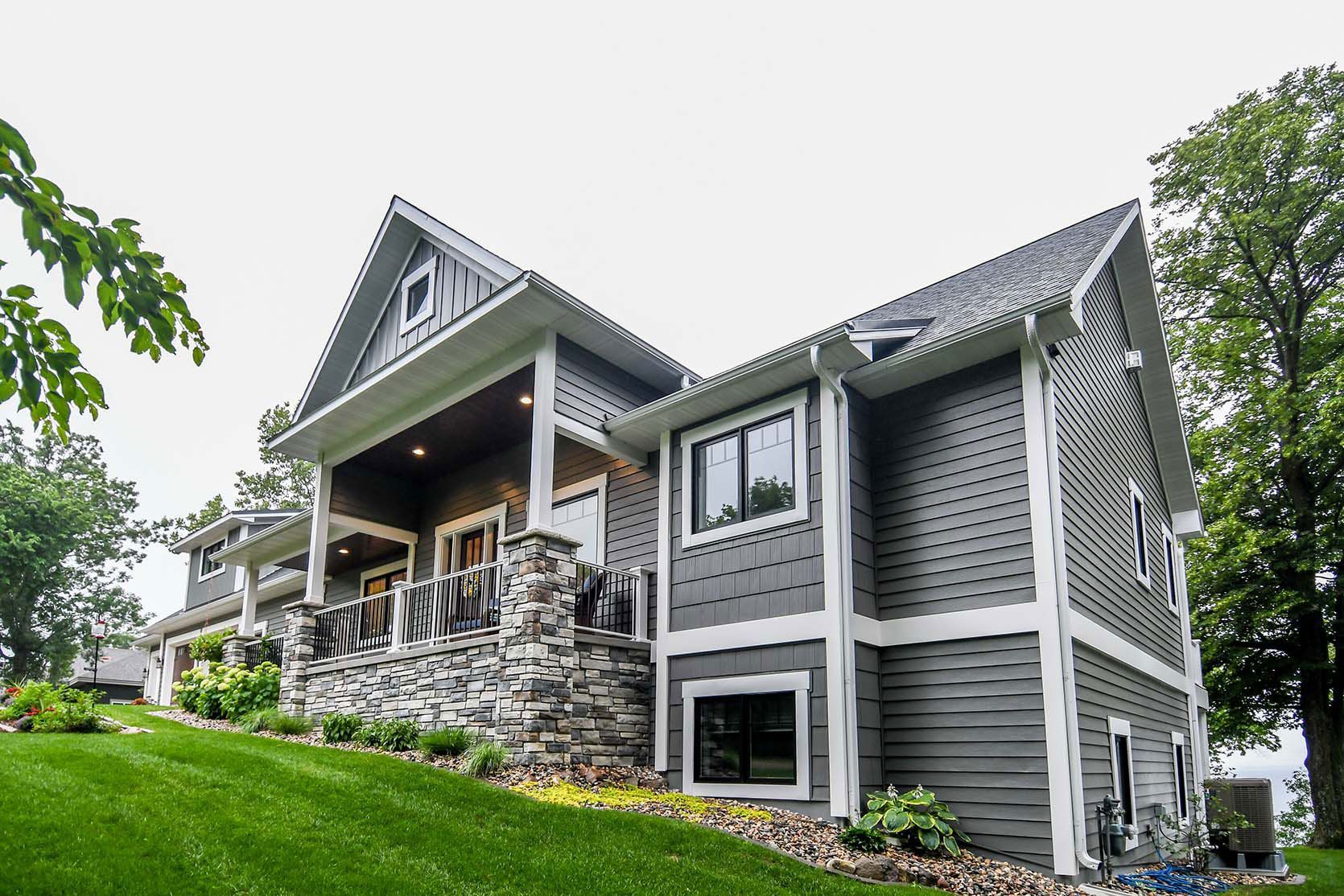 Gray and white house on a hillside with stone accents and a covered porch, green lawn.