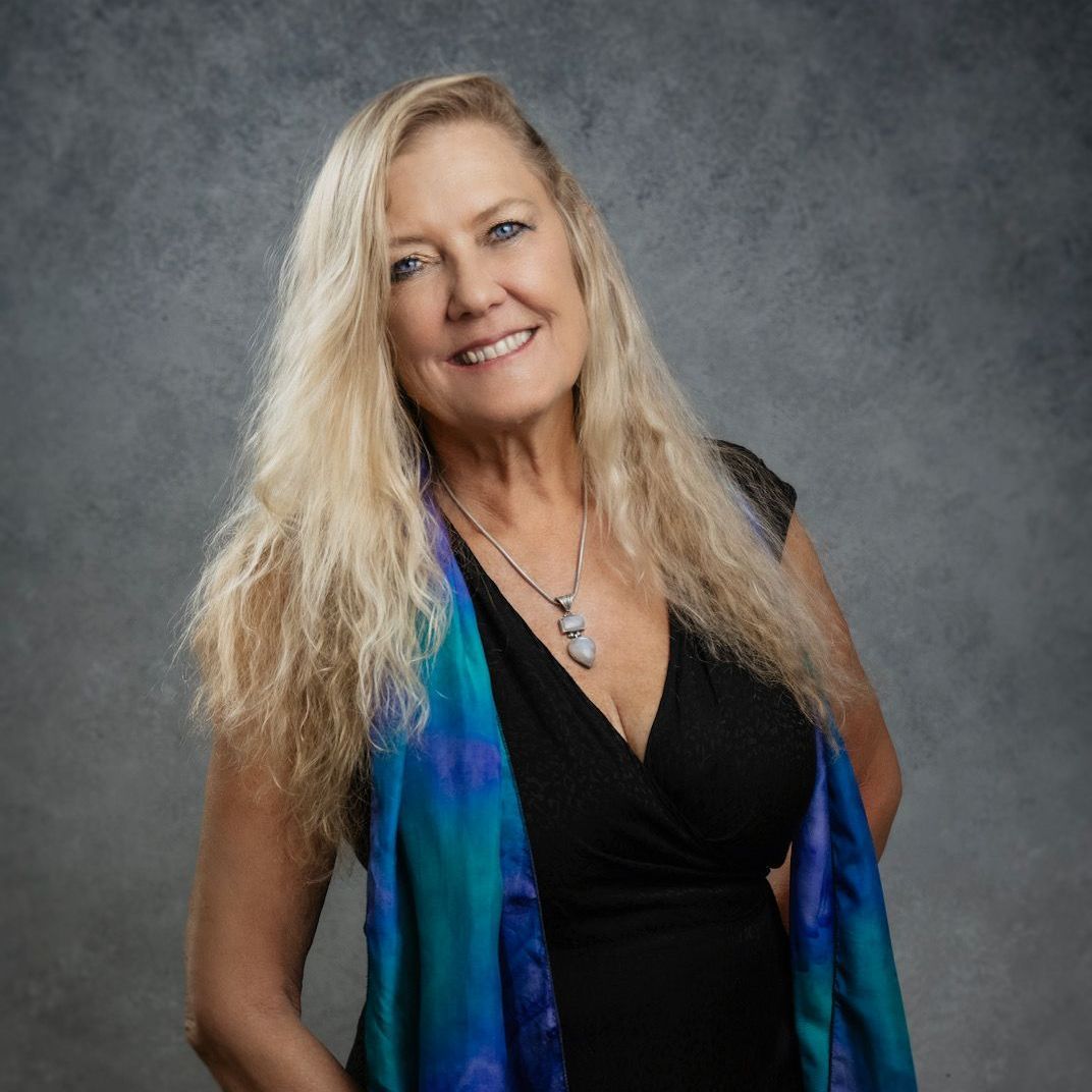 A woman wearing a black dress and a blue scarf is smiling for the camera.