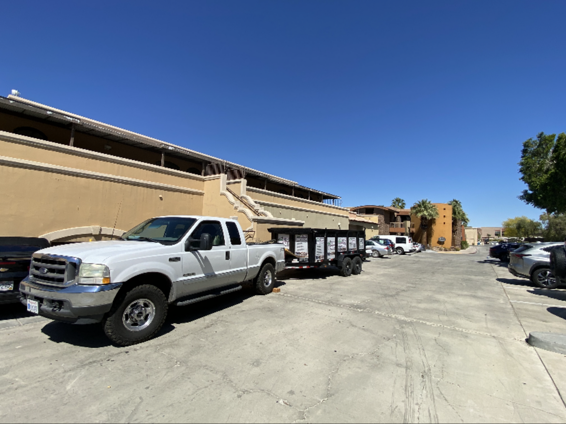 White truck pulling a trailer parked in a lot in front of a tan building under a blue sky. White truck pulling a trailer parked in a lot in front of a tan building under a blue sky.