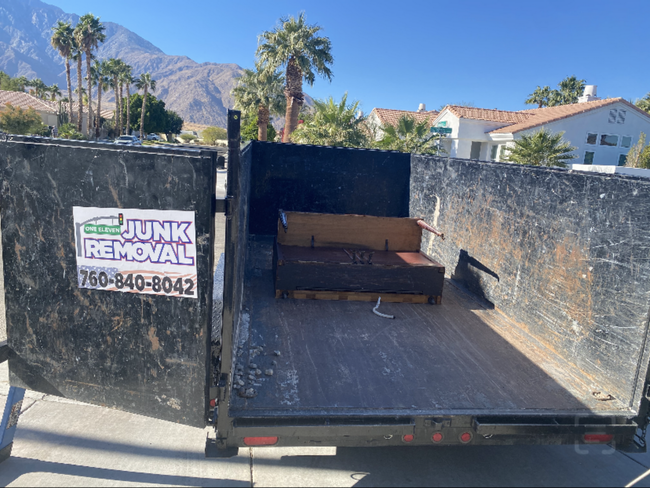 Black dumpster with a partially visible brown sofa, in a residential area with palm trees. Junk removal service. Black dumpster with a partially visible brown sofa, in a residential area with palm trees. Junk removal service.