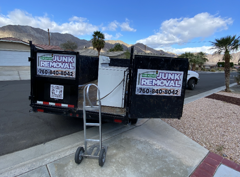 A junk removal trailer with a washing machine, hand truck, and mountain backdrop.