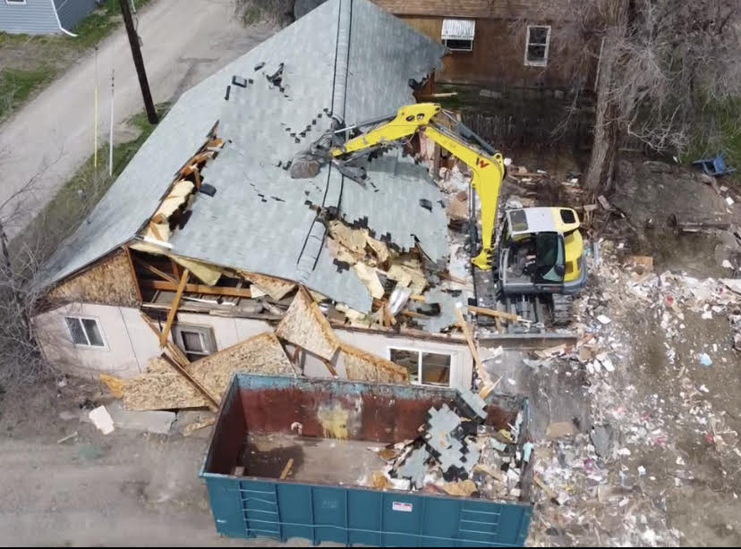 Demolition of a house. An excavator tears down a roof, debris in a dumpster. Outdoors.