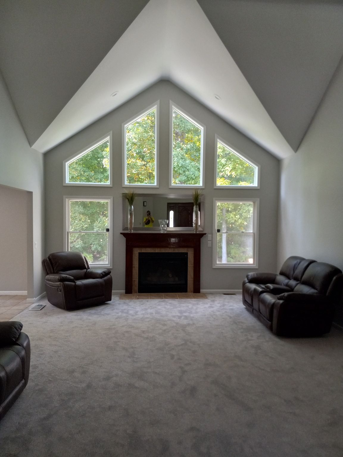 Living room with gray walls, carpet, brown leather furniture, and large windows overlooking trees.