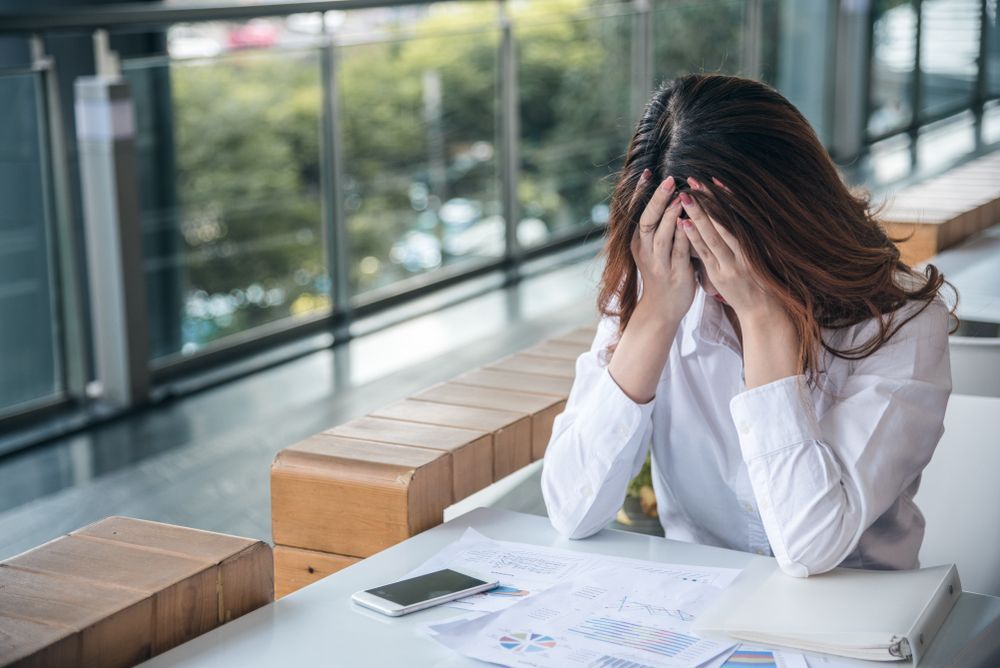 A Person in a White Shirt Sits at a Desk Holding Their Head and Distress — Australian Employee Lawyers in Broadbeach Waters, QLD