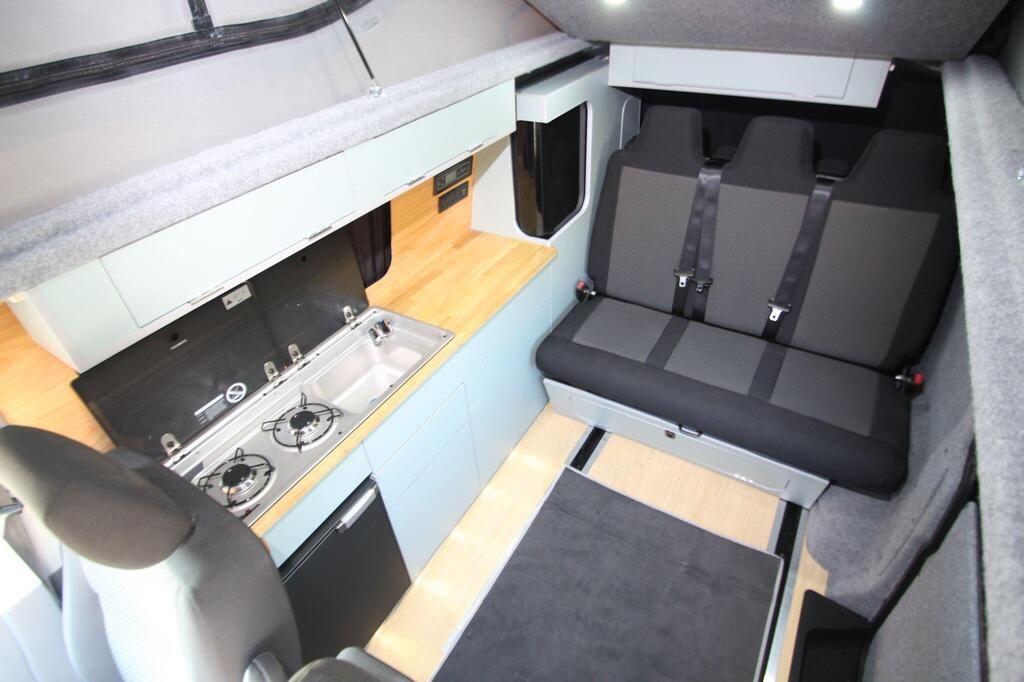 Compact camper van interior with kitchen, seating bench, and table in gray and wood tones