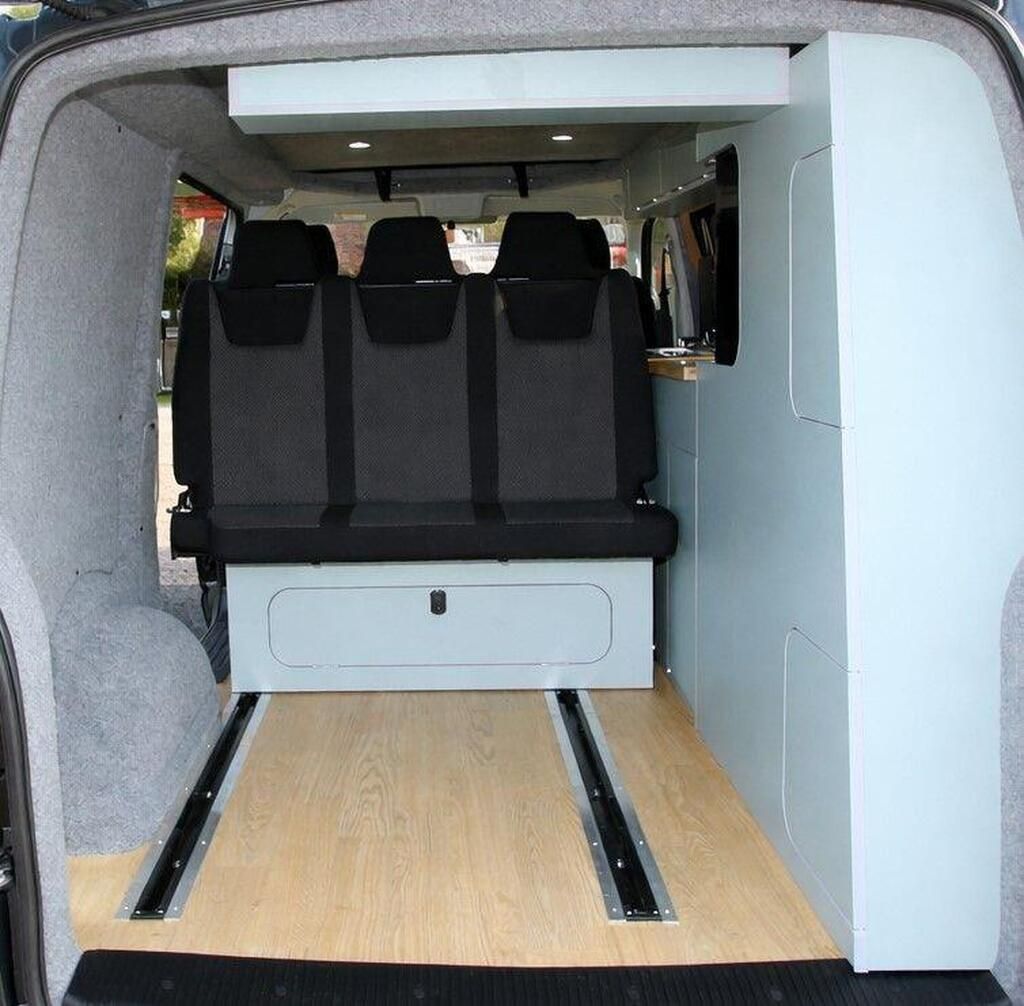 Empty van interior with black rear seats and a light wood floor cargo conversion