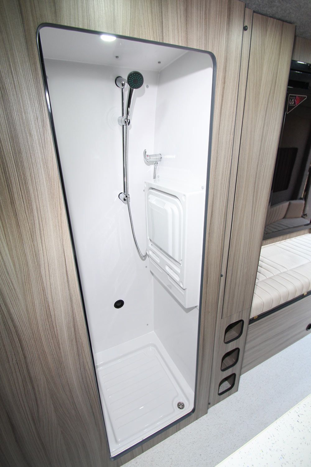 Compact shower stall with white walls, chrome showerhead, handheld sprayer, and built-in shelf in a wood-paneled interior
