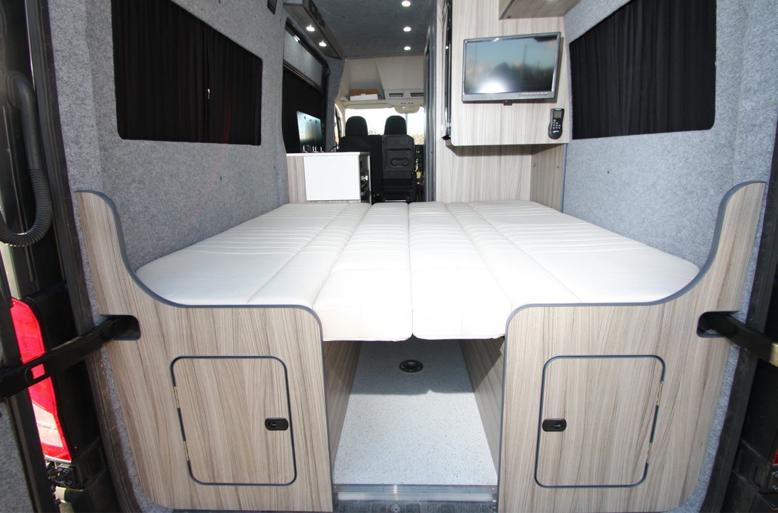 Interior of a camper van with a white bed platform and light wood paneling