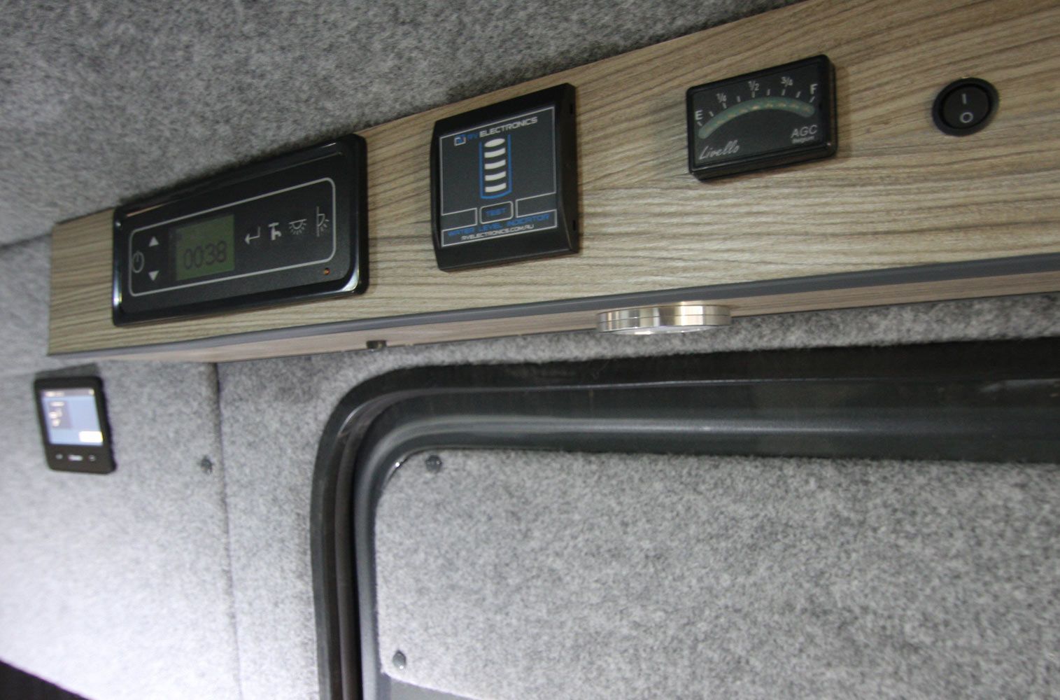 RV interior wall with mounted gauges, control panels, and a small monitor above a window