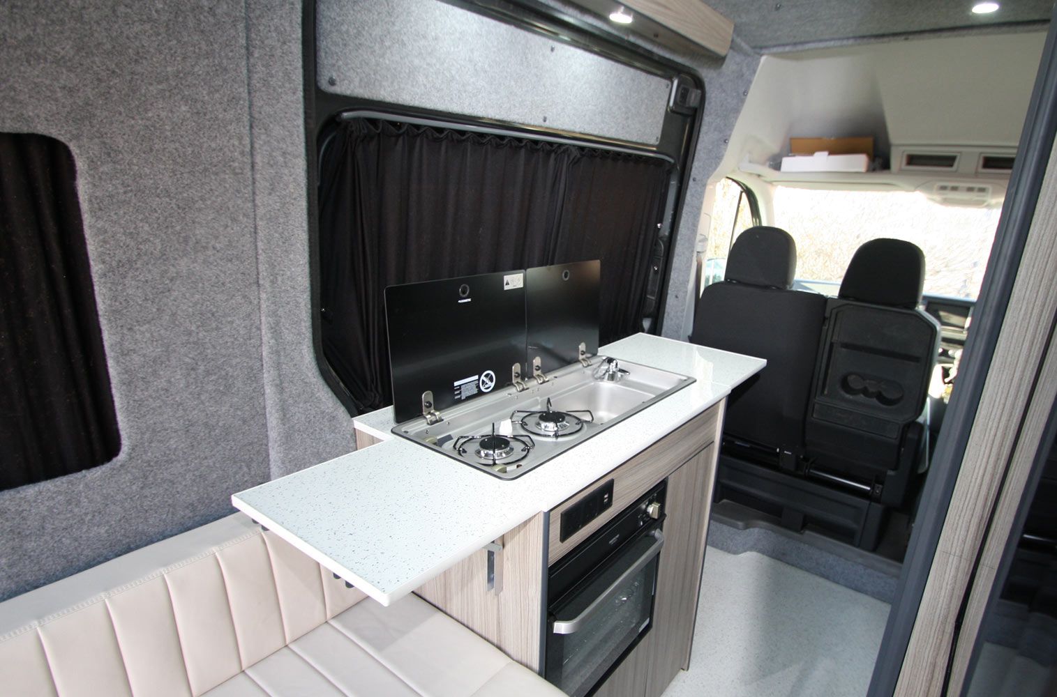 Compact camper van interior with white countertop, stove, sink, and rear seats visible