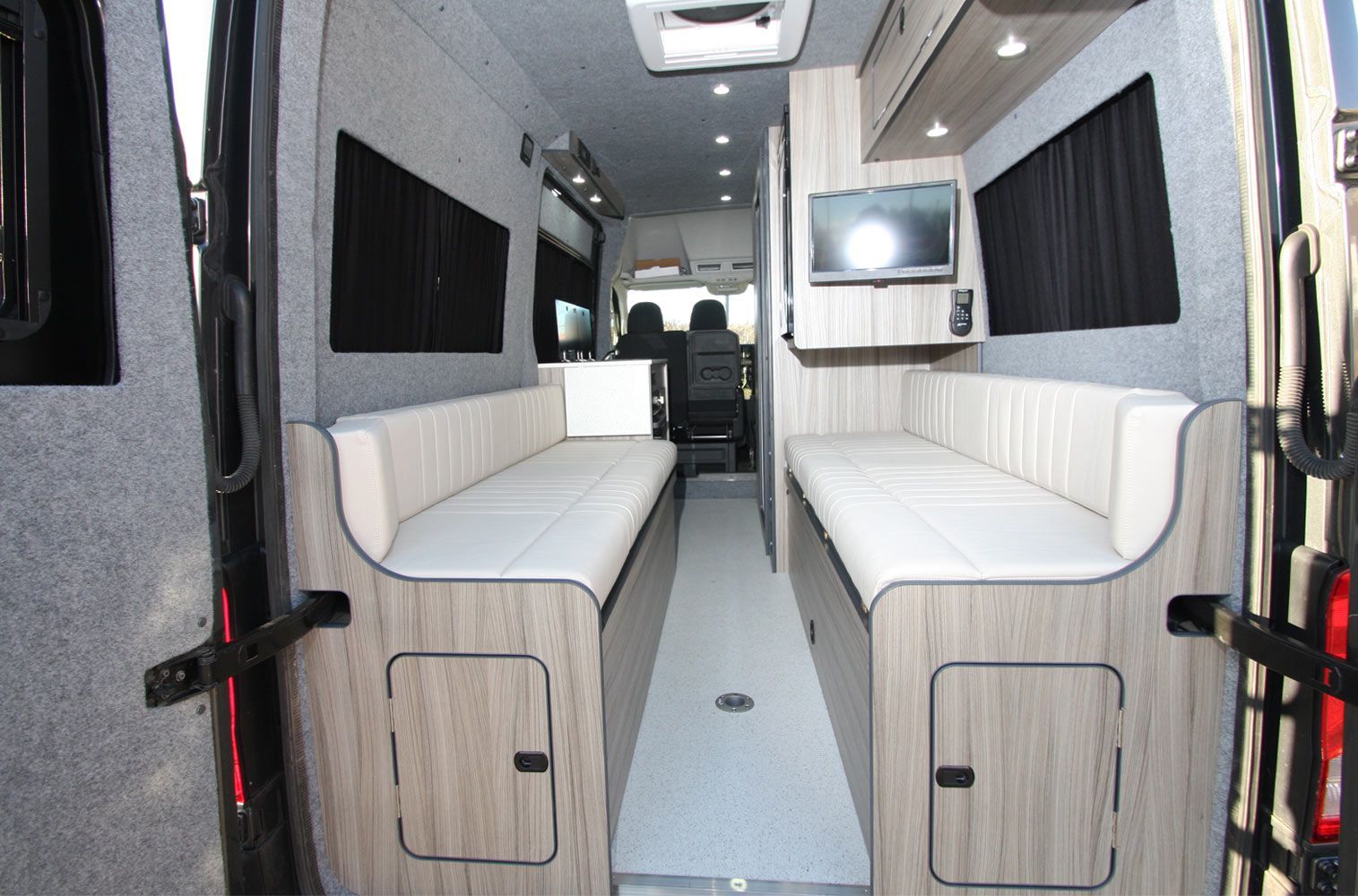Interior of a narrow van with two white bench seats facing each other and a central aisle