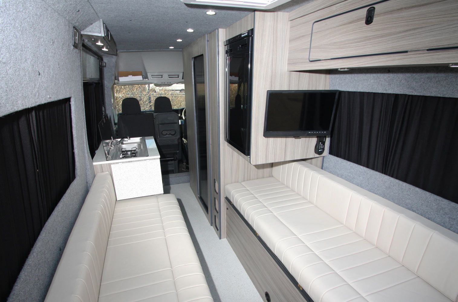 Modern RV interior with white benches, a table, and a view toward the cab area