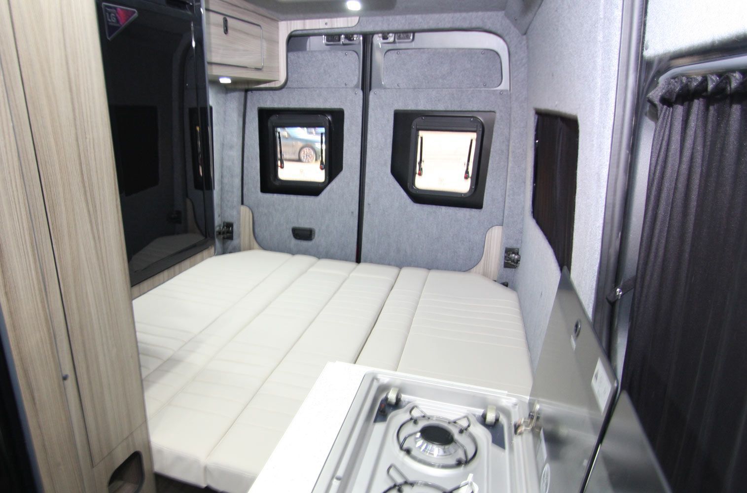 White bunk bed inside a compact camper or RV interior with two small windows and a sink in the foreground