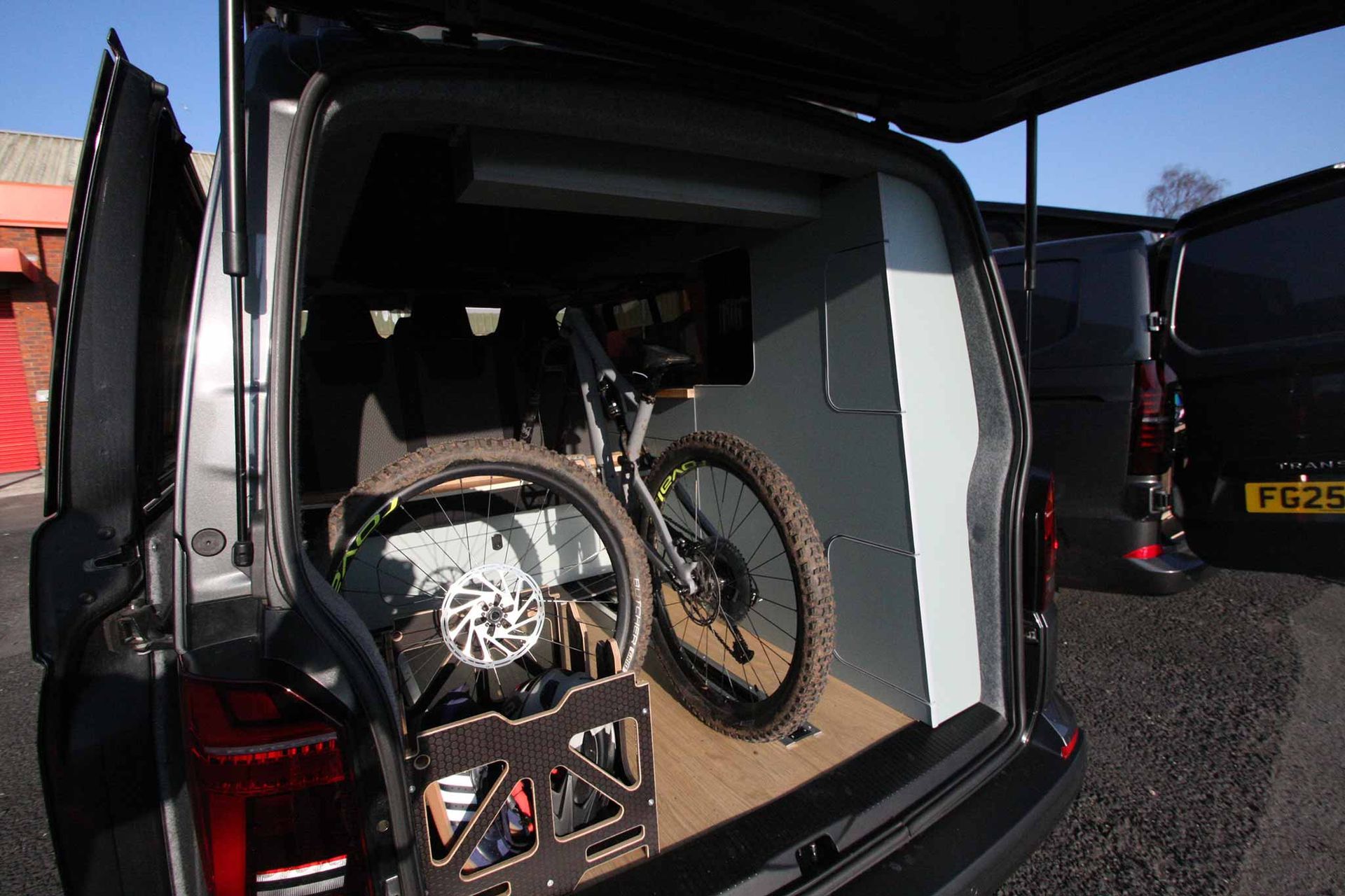 Two mountain bikes loaded in the back of a black van at an outdoor event.