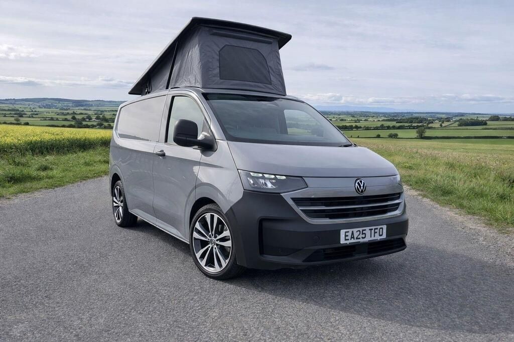Gray camper van parked on a rural road, with a raised pop-top roof and countryside hills behind it
